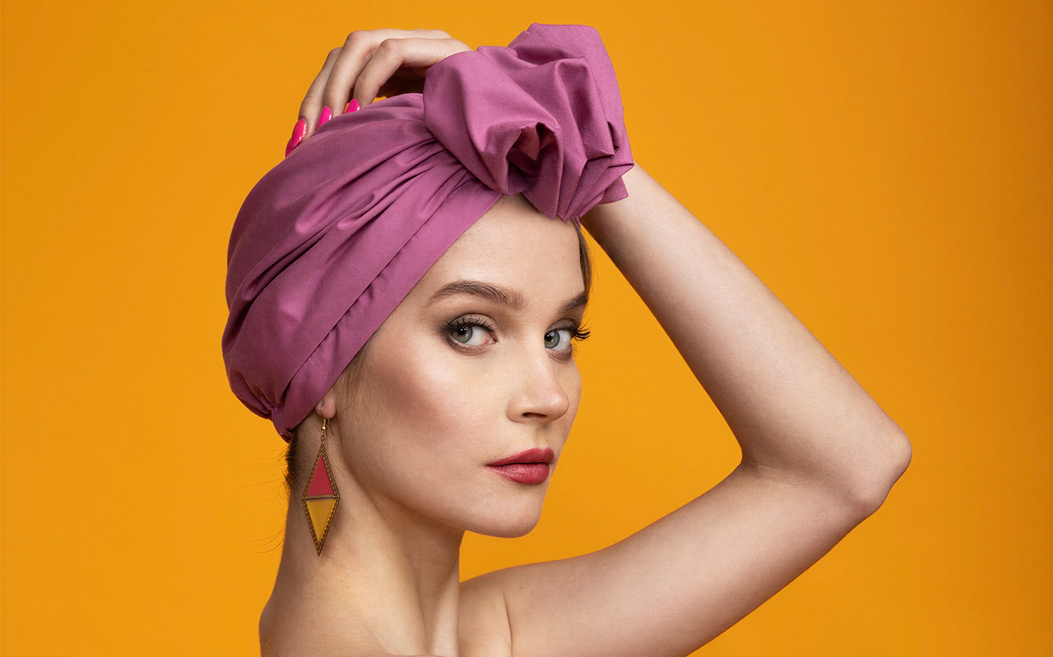 Model wearing the Orchid turban, hand resting on the crown, against a marigold wall